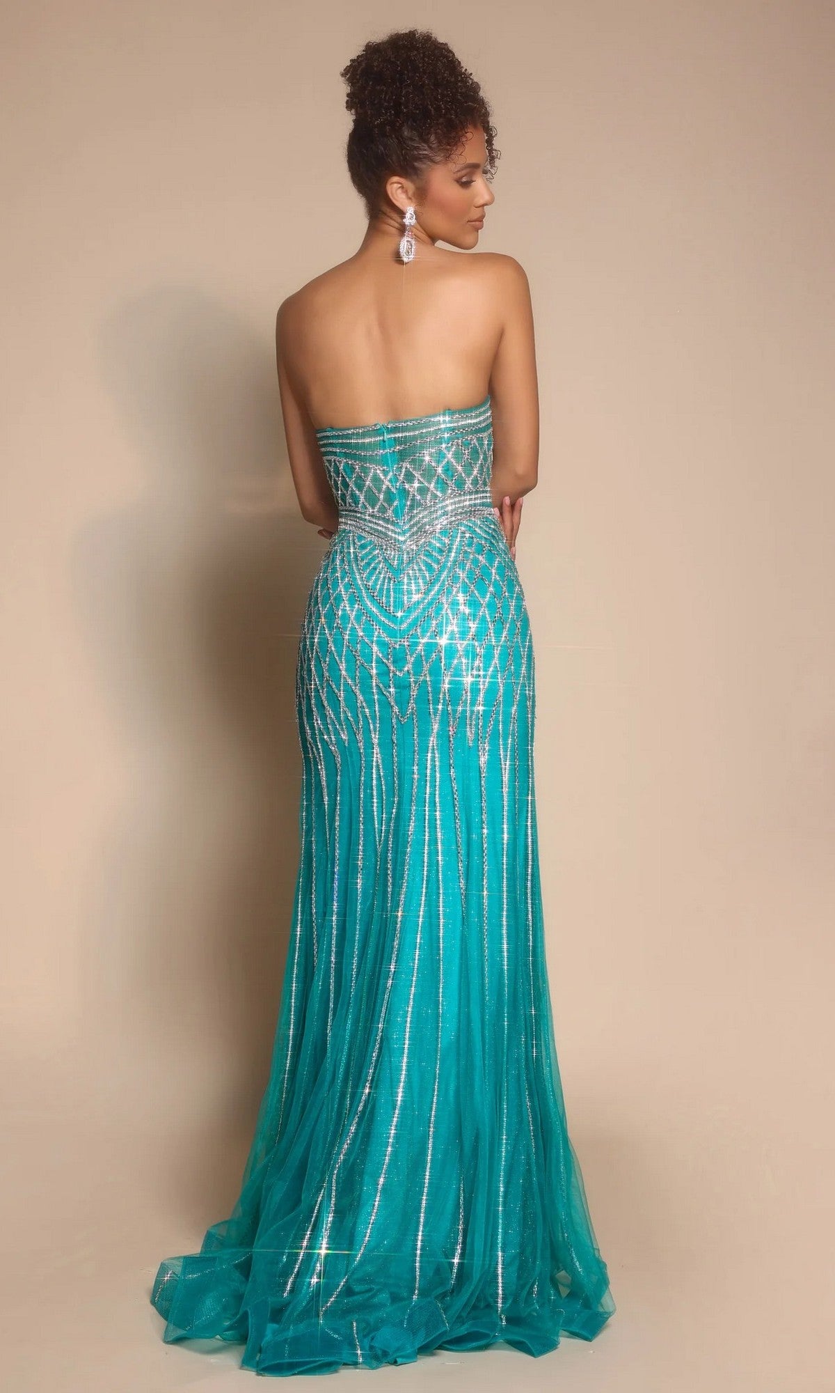 A woman faces away, wearing the Portia and Scarlett PS26072 long formal dress—strapless, turquoise, with sparkling bead embellishments and a sheer floor-length skirt—set against a plain beige background.